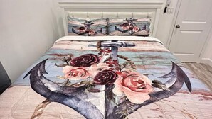 A bedroom with a bed featuring a floral and nautical themed bedspread, a white headboard, and a door to the right. - Anchor Villa: 5 min walk or rent a bike to go to turtle beach. (Exuma)