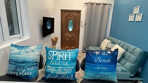 A room with a ceiling fan, an air conditioning unit, a window with a view, a door, a blue wall with framed pictures, and a sofa with decorative pillows. - Anchor Villa: 5 min walk or rent a bike to go to turtle beach. (Exuma)