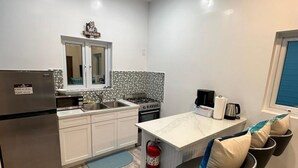 A compact kitchen with white cabinets, a stainless steel refrigerator, a gas stove, and a small island with bar stools. - Anchor Villa: 5 min walk or rent a bike to go to turtle beach. (Exuma)