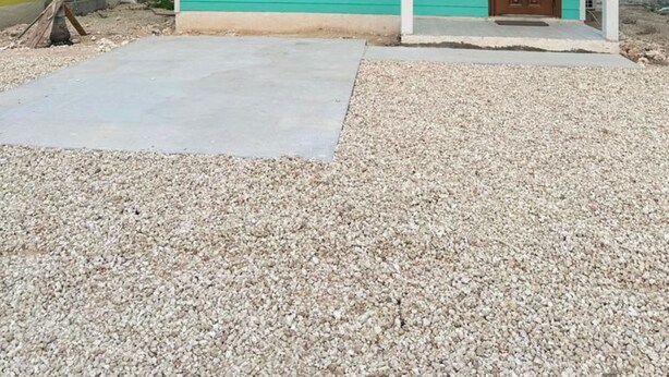 A single-story house with a teal exterior and a brown door, featuring a small porch and a gravel driveway. - Anchor Villa: 5 min walk or rent a bike to go to turtle beach. (Exuma)