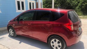A red compact car parked in front of a blue building with white trim. - Anchor Villa: 5 min walk or rent a bike to go to turtle beach. (Exuma)