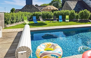 A swimming pool with lounge chairs, a wooden deck, and a stone building in the background. - Lovely home in Canihuel with heated swimming pool (Canihuel)