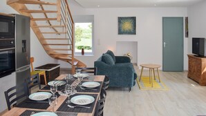 Un espace de vie moderne comprenant un escalier en colimaçon, un coin repas avec une table dressée pour quatre personnes, un canapé et un téléviseur.