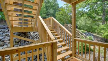 Un escalier en bois mène à une terrasse d’où l’on peut admirer un paysage boisé.