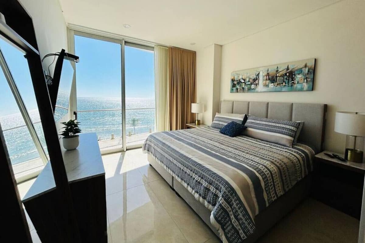 A modern bedroom with a large bed, a city view, and a painting on the wall.