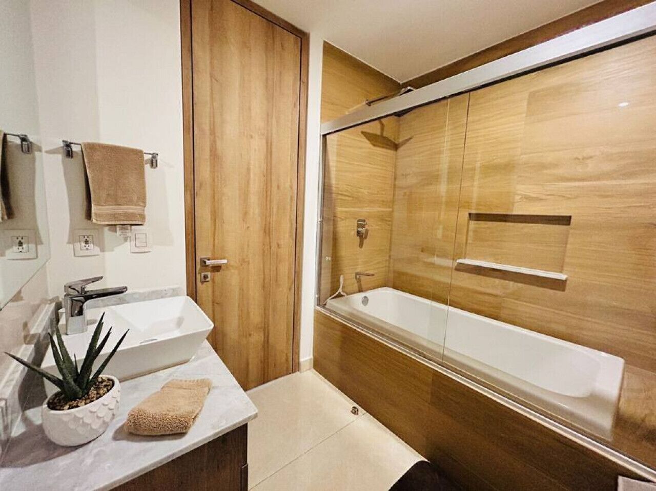 Ein modernes Badezimmer mit einem Holzkosmetikschrank, einem weißen Waschbecken und einer Badewanne.
