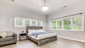 Ein Schlafzimmer mit einem Bett, einem Nachttisch, einem Sessel und großen Fenstern.