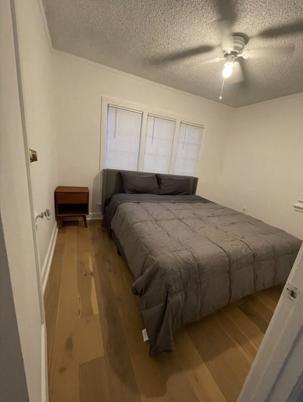 A bedroom with a bed, a nightstand, a ceiling fan, and a window with blinds.