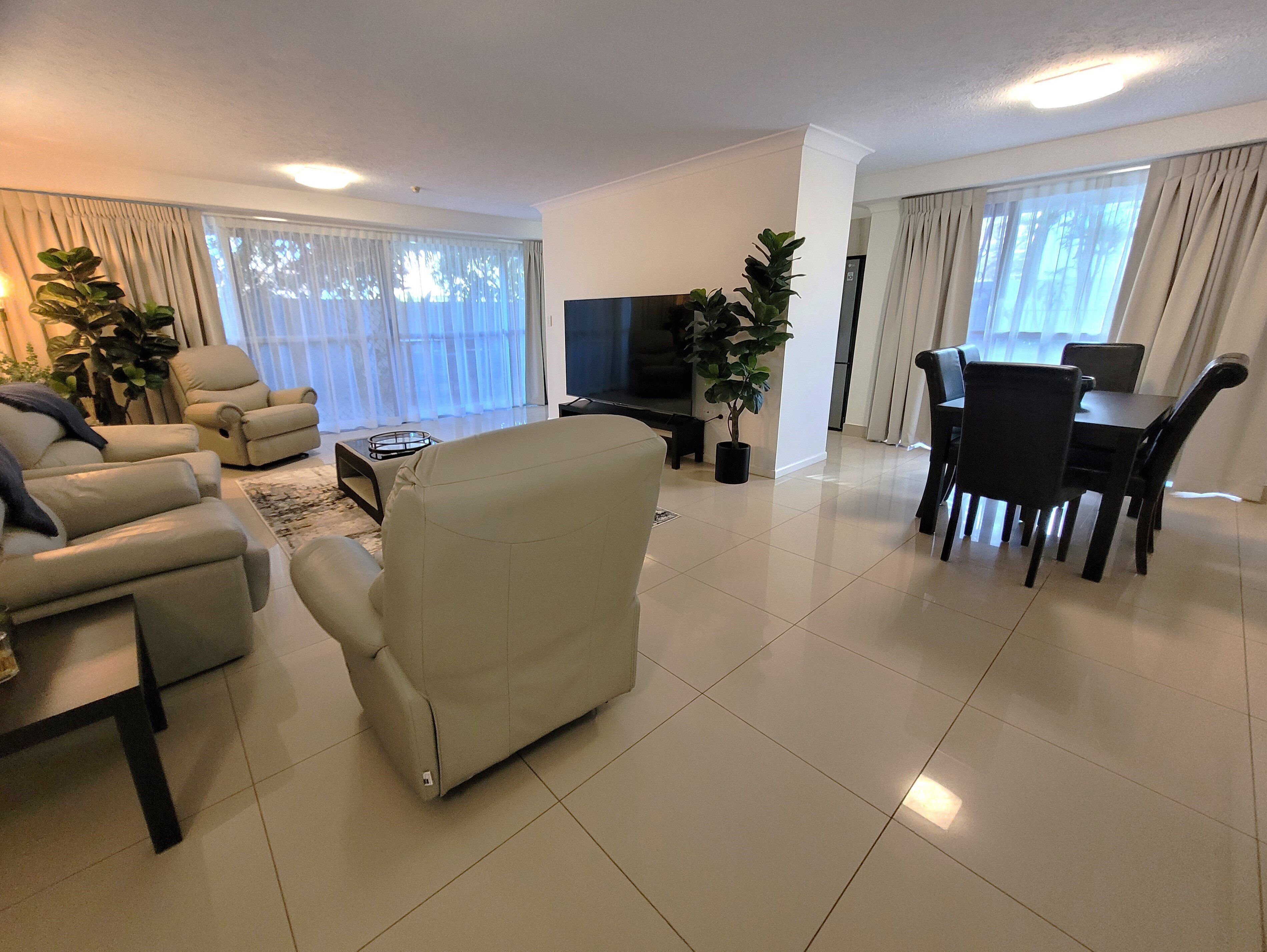 A modern living room with a sofa, TV, dining table, chairs, and potted plants.