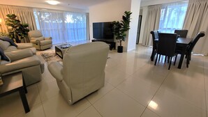 Un salon moderne comprenant un canapé, un téléviseur, une table à manger, des chaises et des plantes en pot.
