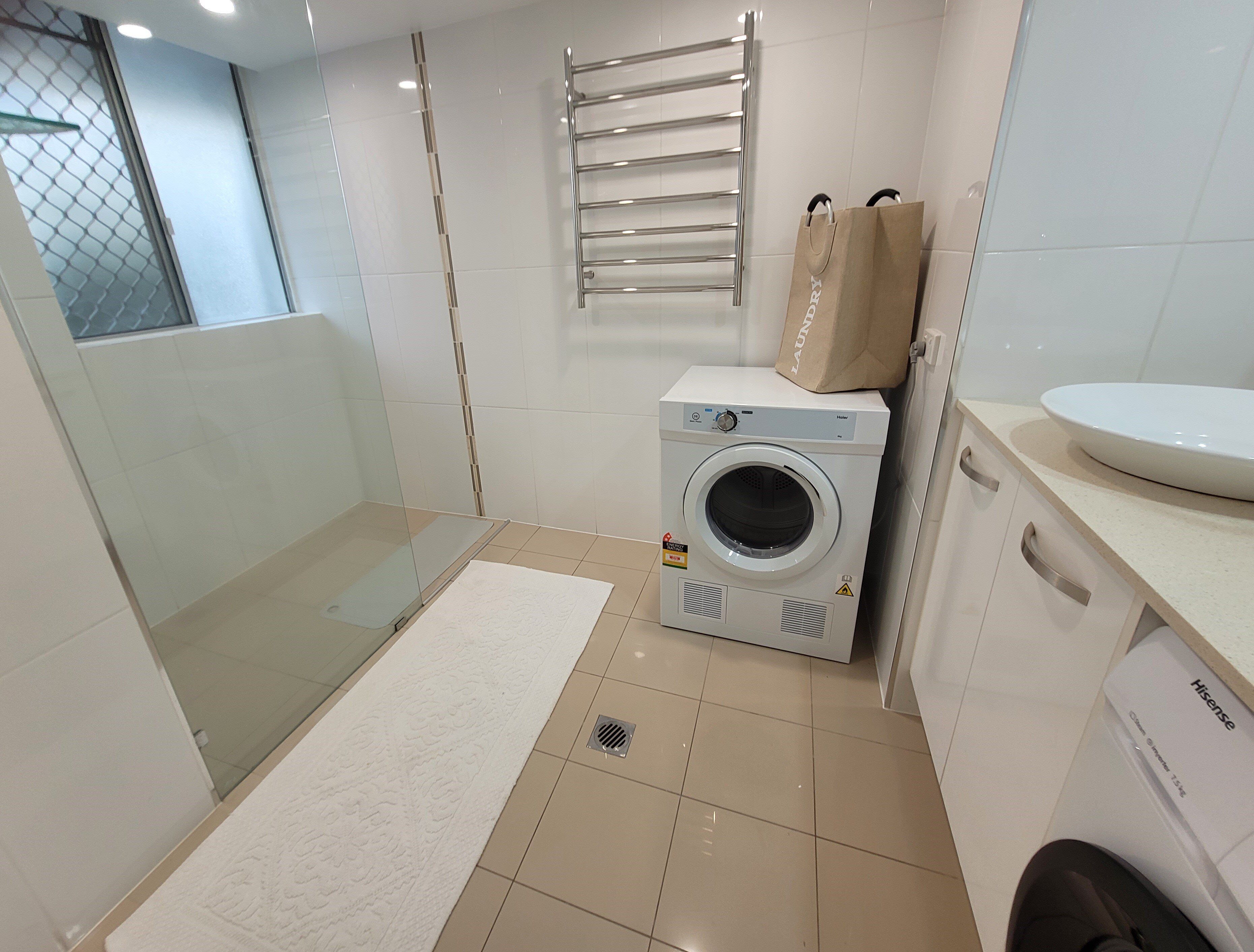Um banheiro compacto com cabine de chuveiro de vidro, máquina de lavar embutida, porta-toalhas e pia com espelho.