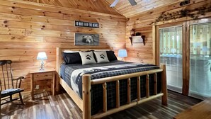 Ein Schlafzimmer einer Holzhütte mit einem Bett, zwei Nachttischen, einem Deckenventilator und einem Fenster mit Jalousien.