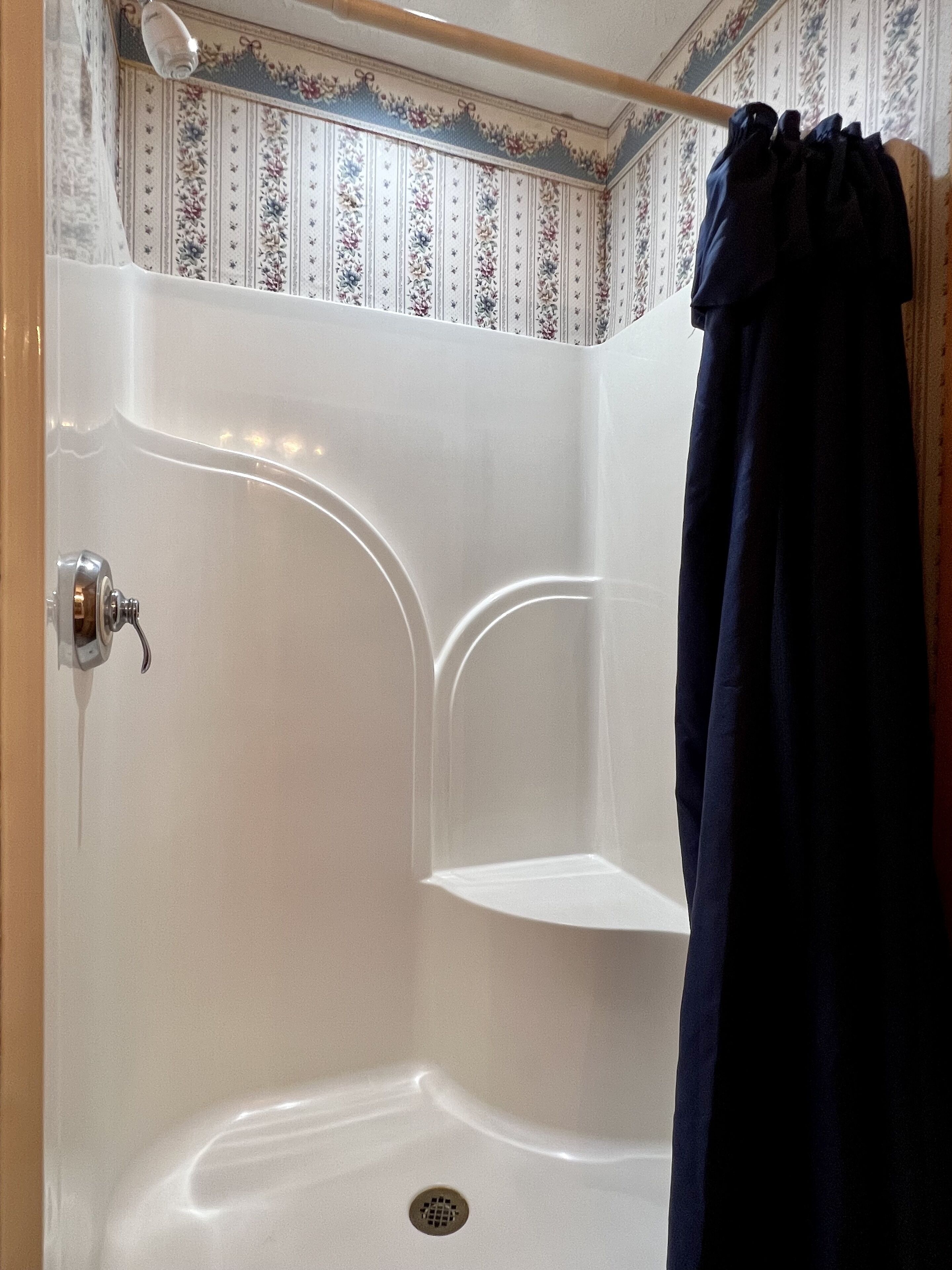A corner shower with a white tiled wall, a showerhead, and a dark blue shower curtain.