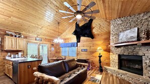 Ein Blockhaus-Interieur mit Holzbalkendecke, Kamin aus Stein, Essbereich und Küche.