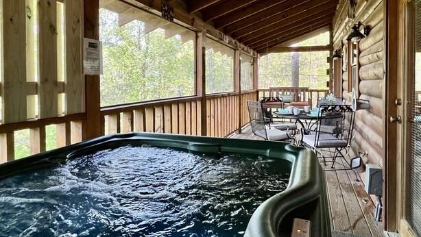 Eine Holzterrasse mit Whirlpool, Sitzgelegenheiten im Freien und Blick auf Bäume.