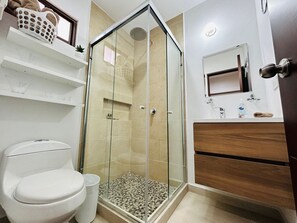 Un baño moderno con ducha de vidrio, inodoro y tocador con espejo.