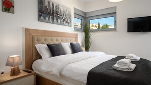 Un letto rifatto con cura, con biancheria da letto bianco e nero, una testiera in legno e un comodino con lampada e telecomando.