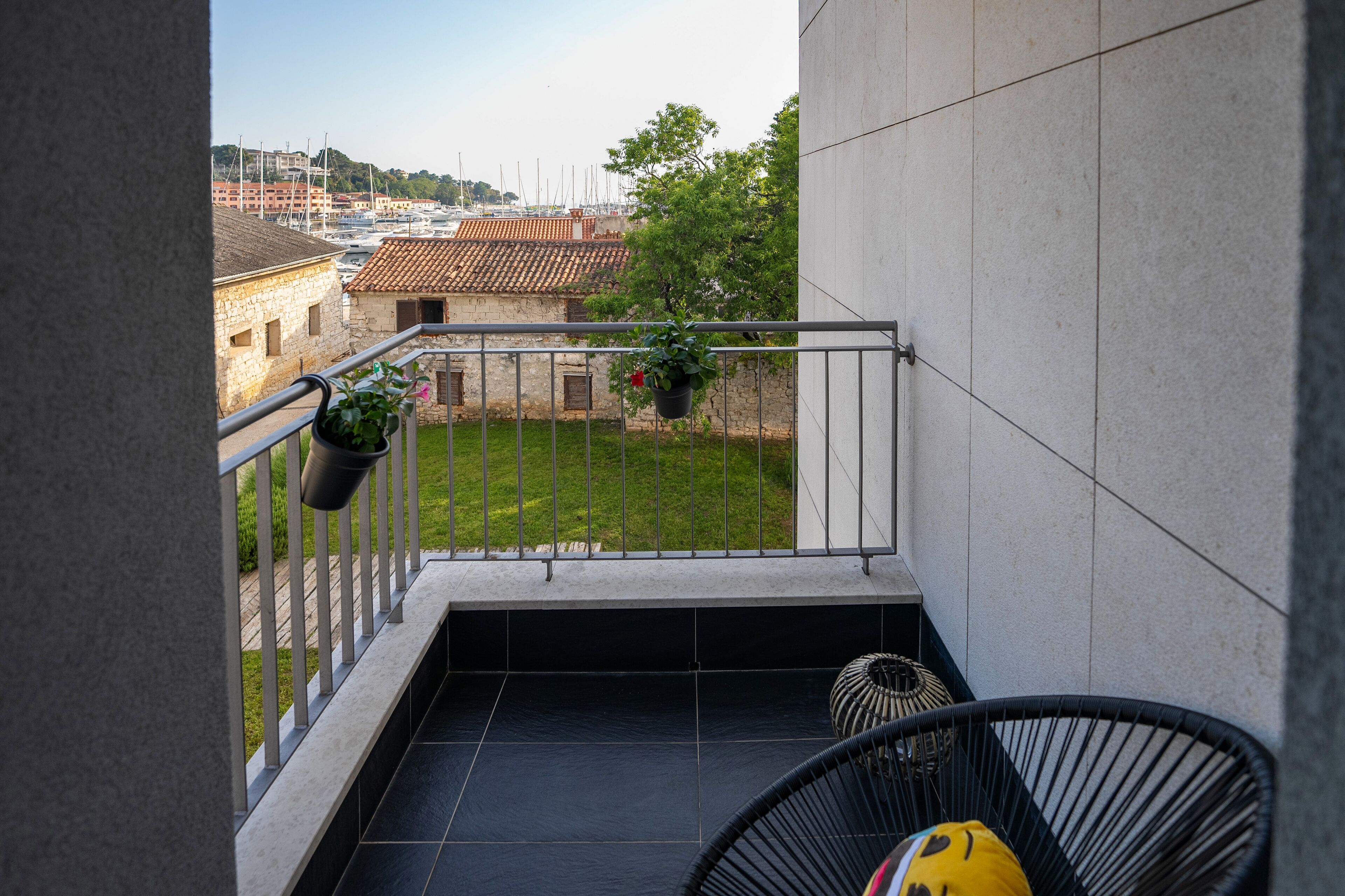 A balcony with a view of a marina, a hanging plant, and a black chair.