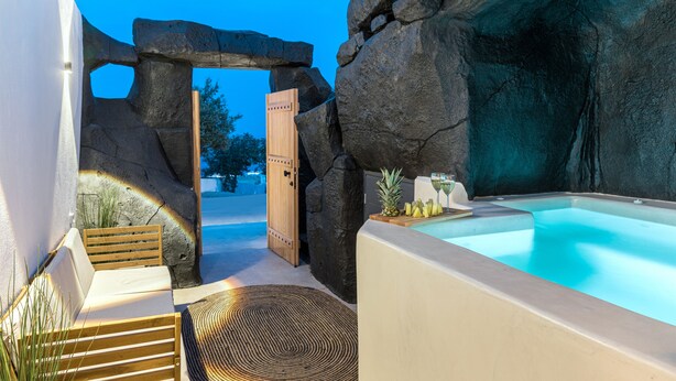 Un espace de détente avec un jacuzzi, des sièges en bois et une arche en pierre.