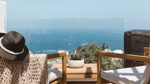 Un balcon avec vue sur la mer, une chaise en bois, un coussin, un article tricoté et une plante en pot.