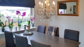 Ein Essbereich mit Tisch, Stühlen, einer Chandelier und Topfpflanzen.