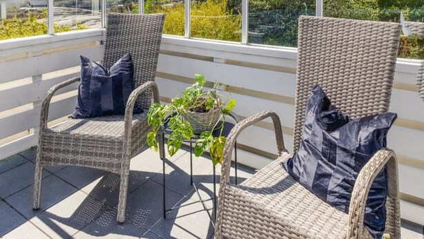 Zwei Korbstühle mit dunklen Kissen, ein kleiner Tisch mit einem Blumentopf und ein Blick auf Grün hinter einem Fenster.