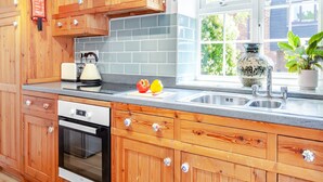 A kitchen with wooden cabinets, a toaster, a kettle, a sink, and a window with a view of greenery. - A stunning one bedroom property in a great location with some fantastic views. (Hailsham)