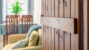 A cozy living room with a wooden wall, a sofa, a table with chairs, and a view of the outside. - A stunning one bedroom property in a great location with some fantastic views. (Hailsham)