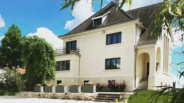 A two-story building with a symmetrical facade, a central entrance with steps, and a balcony on the upper floor. - Luxury villa pool for 20 people (Montureux-lès-Baulay)