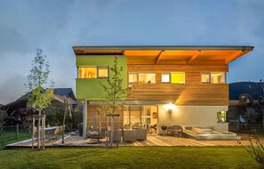 Une maison moderne à deux étages, dotée d’un toit plat, de grandes fenêtres et d’un patio extérieur bien éclairé.