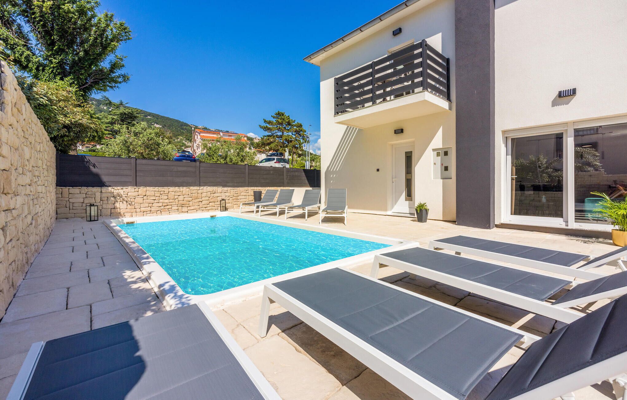 En modern villa med en swimmingpool, solstolar och en stenmur.