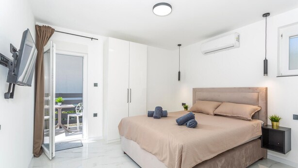 Et moderne soveværelse med en stor seng, en balkon med udsigt og et ophængt tv.