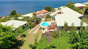 A residential area with a swimming pool, houses, and a view of the ocean. - Villa Frangipanier with private pool (Case-Pilote)