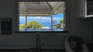 A kitchen with a window overlooking a scenic view of the ocean and a garden. - Villa Frangipanier with private pool (Case-Pilote)