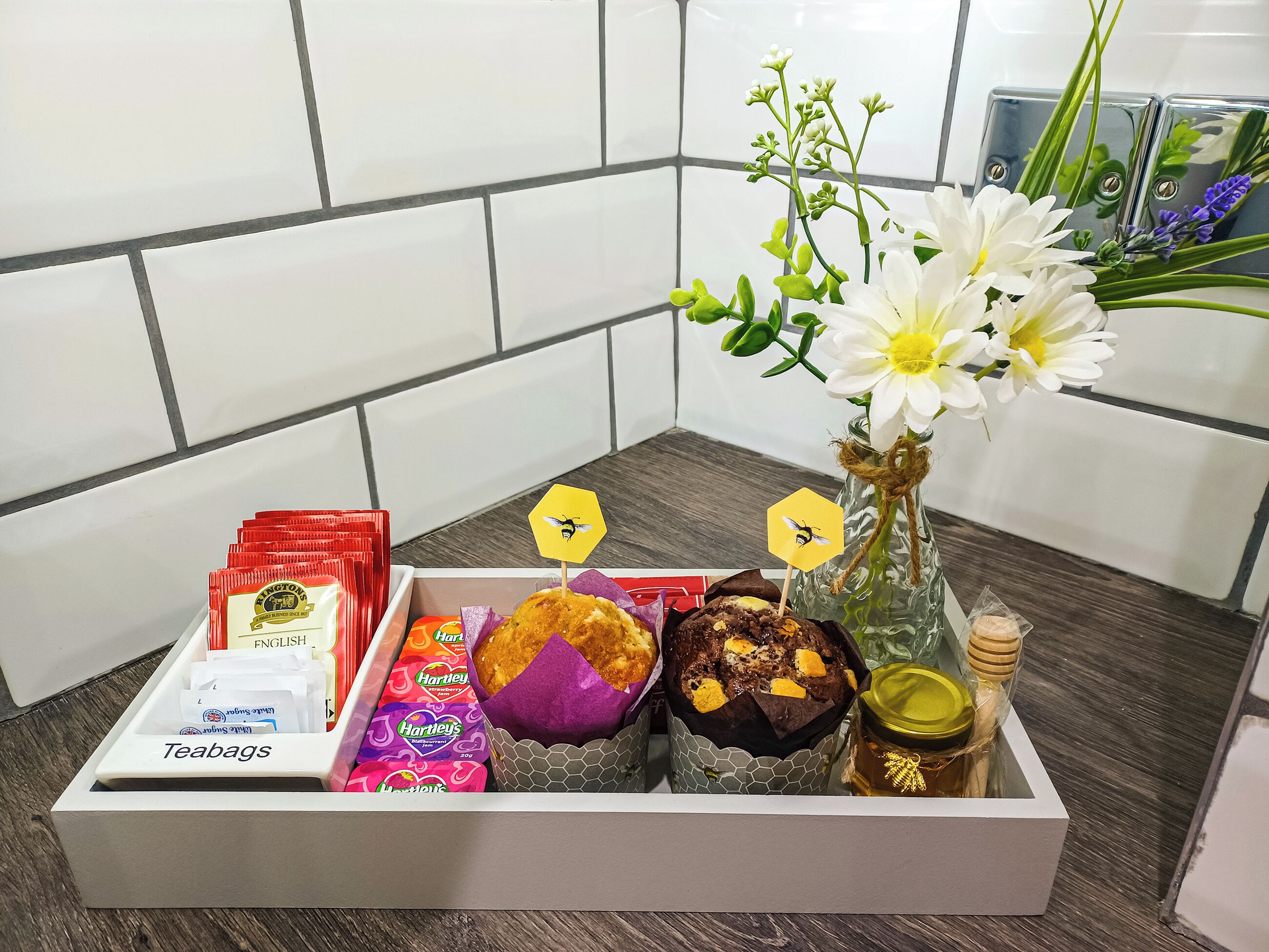 En bakke med teposer, muffins og en vase med blomster.