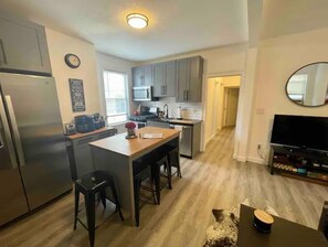A modern kitchen with grey cabinets, a central island with stools, a refrigerator, and a microwave.