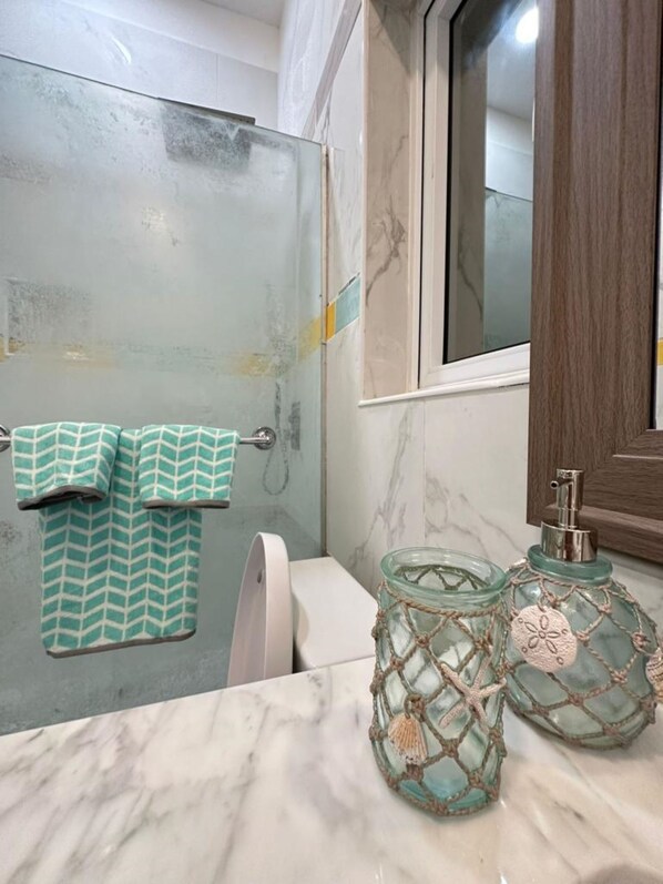 Ein Badezimmer mit Duschabtrennung aus Glas, Toilette, Waschbecken mit Marmorplatte und dekorativen Glasbehältern.