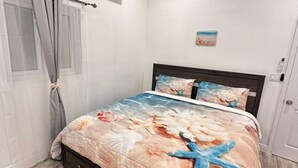 Et soveværelse med seng, aircondition, loftventilator og et sengetæppe med strandtema.