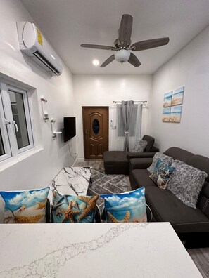 Ein modernes Wohnzimmer mit Deckenventilator, einer Couch, einem Couchtisch und einem Fernseher.