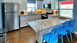 A modern kitchen with white cabinets, stainless steel appliances, a granite countertop, and blue chairs. - Pink Flamingo  (Freeport)