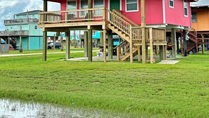 A red house with a wooden deck and stairs, surrounded by green grass and a clear sky. - Pink Flamingo  (Freeport)
