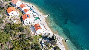 Une vue aérienne d’une zone côtière avec des bâtiments, une plage et des eaux d’un bleu limpide.