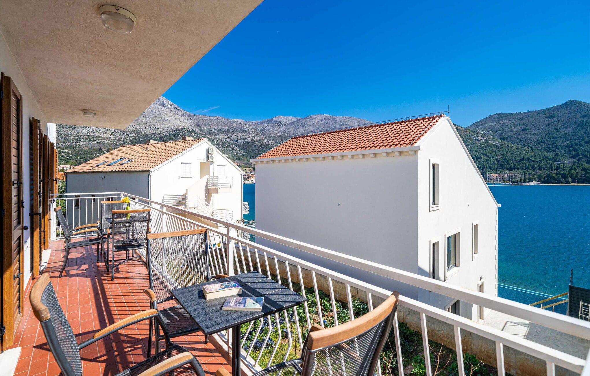 Un balcon avec une table et des chaises, donnant sur un plan d’eau et des montagnes.