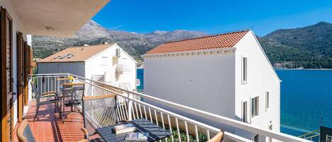A balcony with a table and chairs, overlooking a body of water and mountains.
