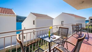 Un balcon avec une table et des chaises, donnant sur une zone côtière où se trouvent des bâtiments à étages.