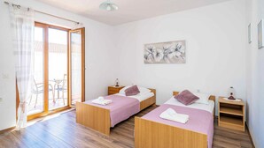 Une chambre avec deux lits, une porte-fenêtre coulissante donnant sur un balcon, un luminaire au plafond et un tableau accroché au mur.