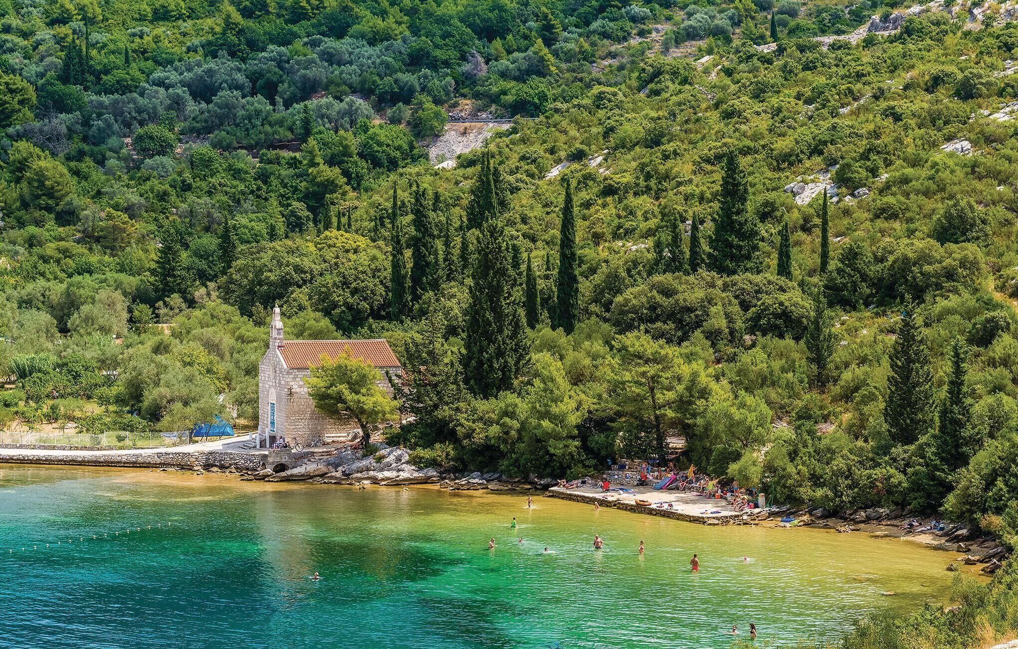A coastal area with a small stone church, clear turquoise waters, and a rocky shoreline.