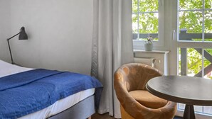 Ein Schlafzimmer mit einem Bett, einem Sessel, einem Tisch und einem Fenster mit Blick auf Grünflächen.