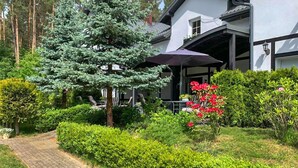 Ein modernes Haus mit einem gepflegten Garten, einem großen Baum und einer Terrasse mit Sitzgelegenheiten.