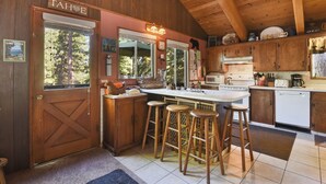 A wooden cabin kitchen with a large island, bar stools, and a view of trees through the windows.